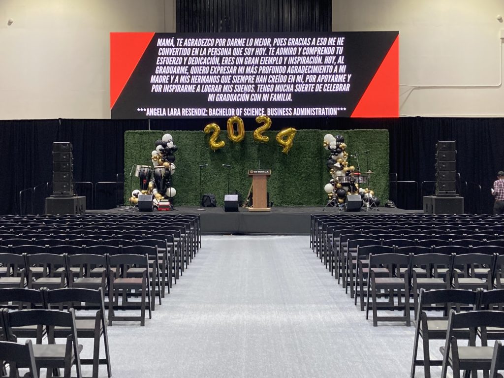 A stage rental set up with a podium, balloons that read '2024', and sound system rentals for a graduation ceremony in Los Angeles