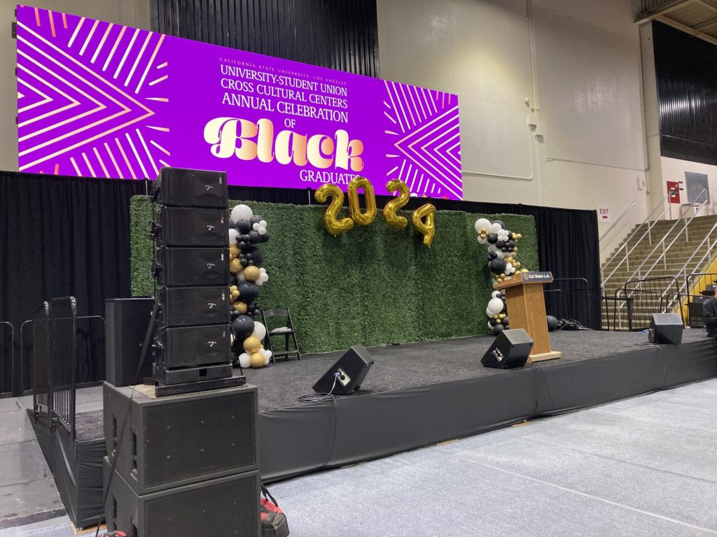 A stage rental set up with a podium, balloons that read '2024', and sound system rentals for a graduation ceremony in Los Angeles