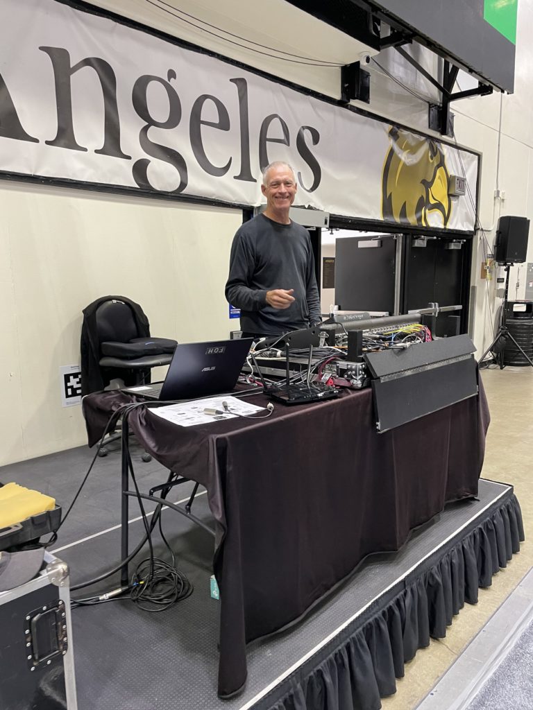 An ELP audiovisual technician poses in front of audio equipment for a graduation ceremony